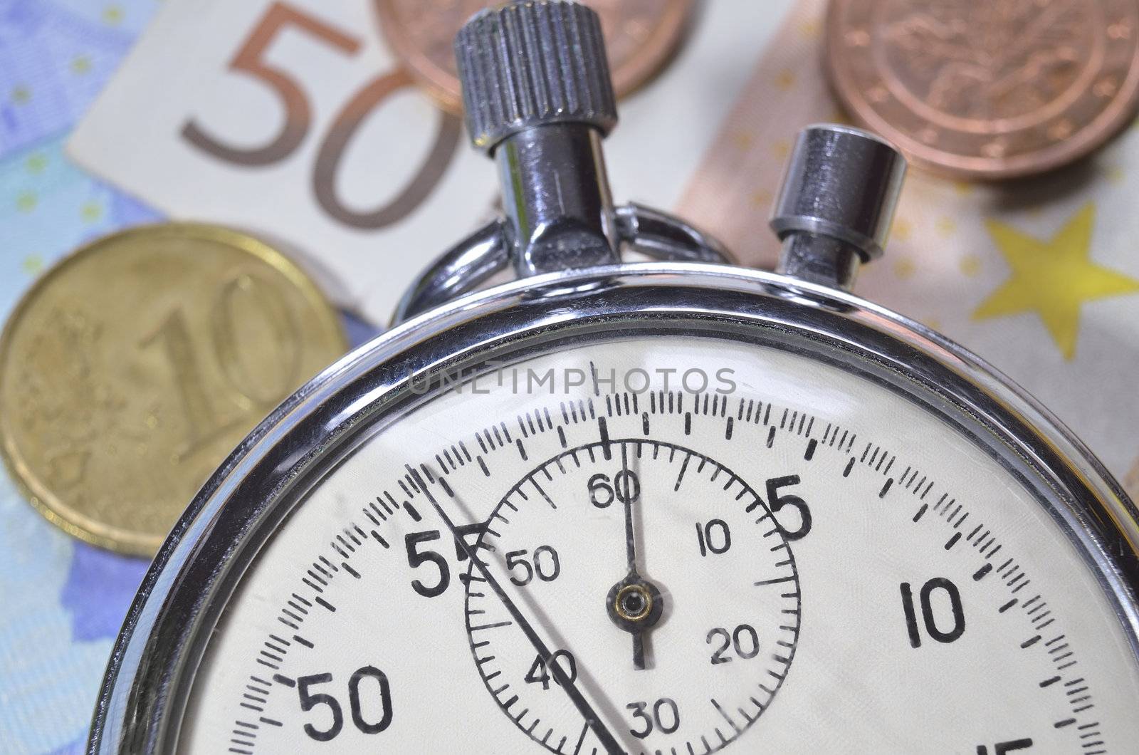 stopwatch lays over Euro coins and  banknotes; focus on watch arrow