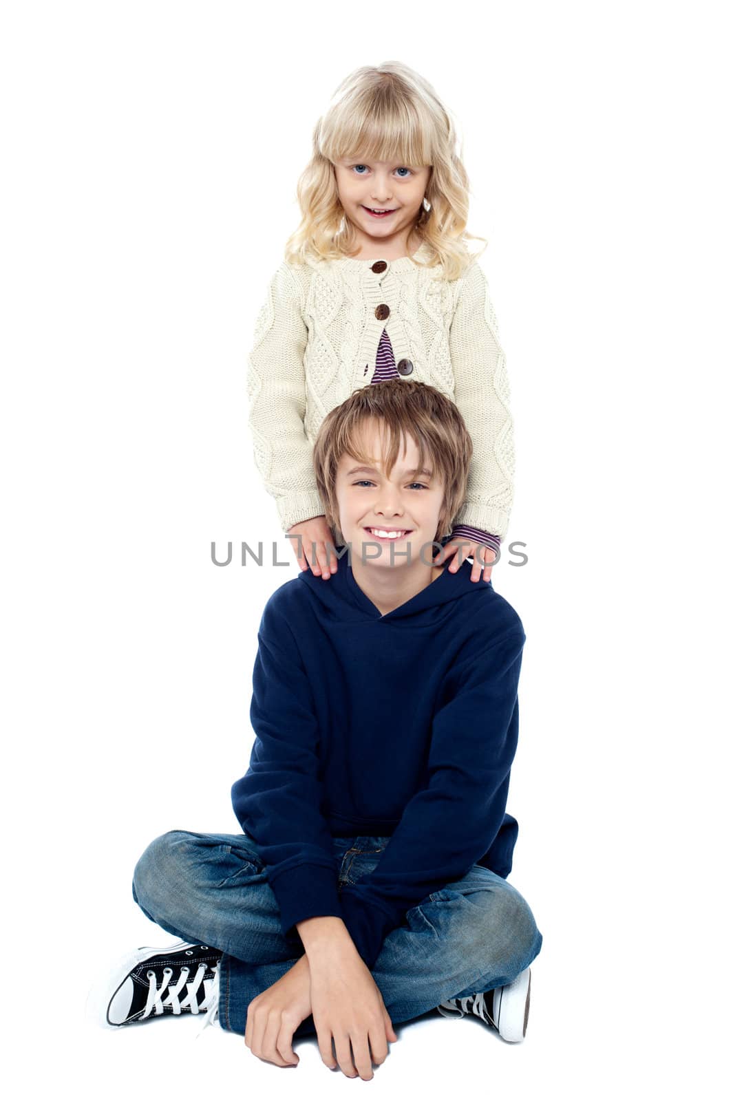 Smart young boy sitting with his legs crossed and his sister standing behind him.