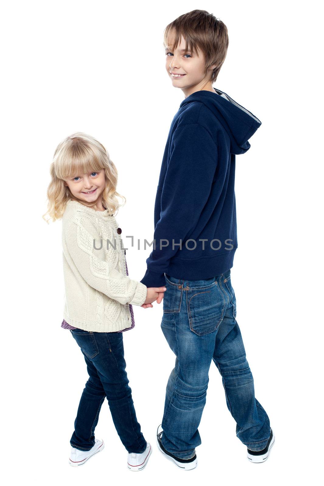 Delightful kids turning back and facing camera. Brother holding sisters hand.