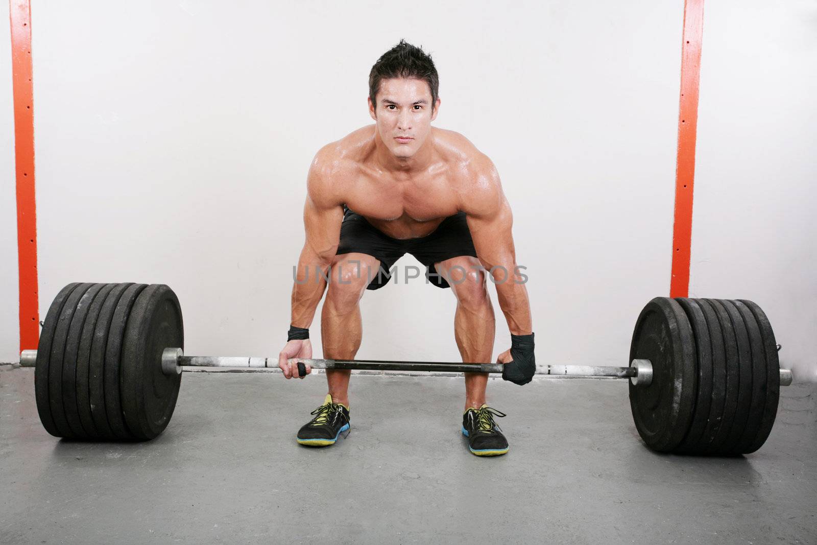 Young and muscular guy holding a barbell. Crossfit dead lift excercise.
