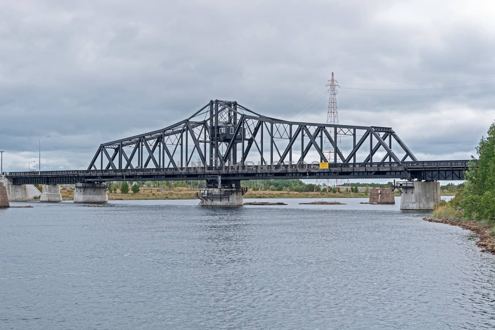 The bridge across a narrow channel separating Manitoulin Island from the much smaller Goat Island, forming the only land access. It consists of two 21 m (70 ft) deck plate girder approaches on the north end (Goat Island) and a single 18 m (60 ft) deck plate girder approach on the south end (Manitoulin Island), with a 112 m (368 ft) through swing bridge span. The swing bridge sits 5.3 m (17.5 ft) above mean water level, and provides a 48 m (160 ft) opening on either side of the central pier for water passage. Construction of the bridge was started by the Algoma Eastern Railway with the abutments and piers being built in 1912 and the bridge structure being erected in 1913. The Algoma Eastern Railway began operating trains across the bridge to the community of Little Current in October 1913. 