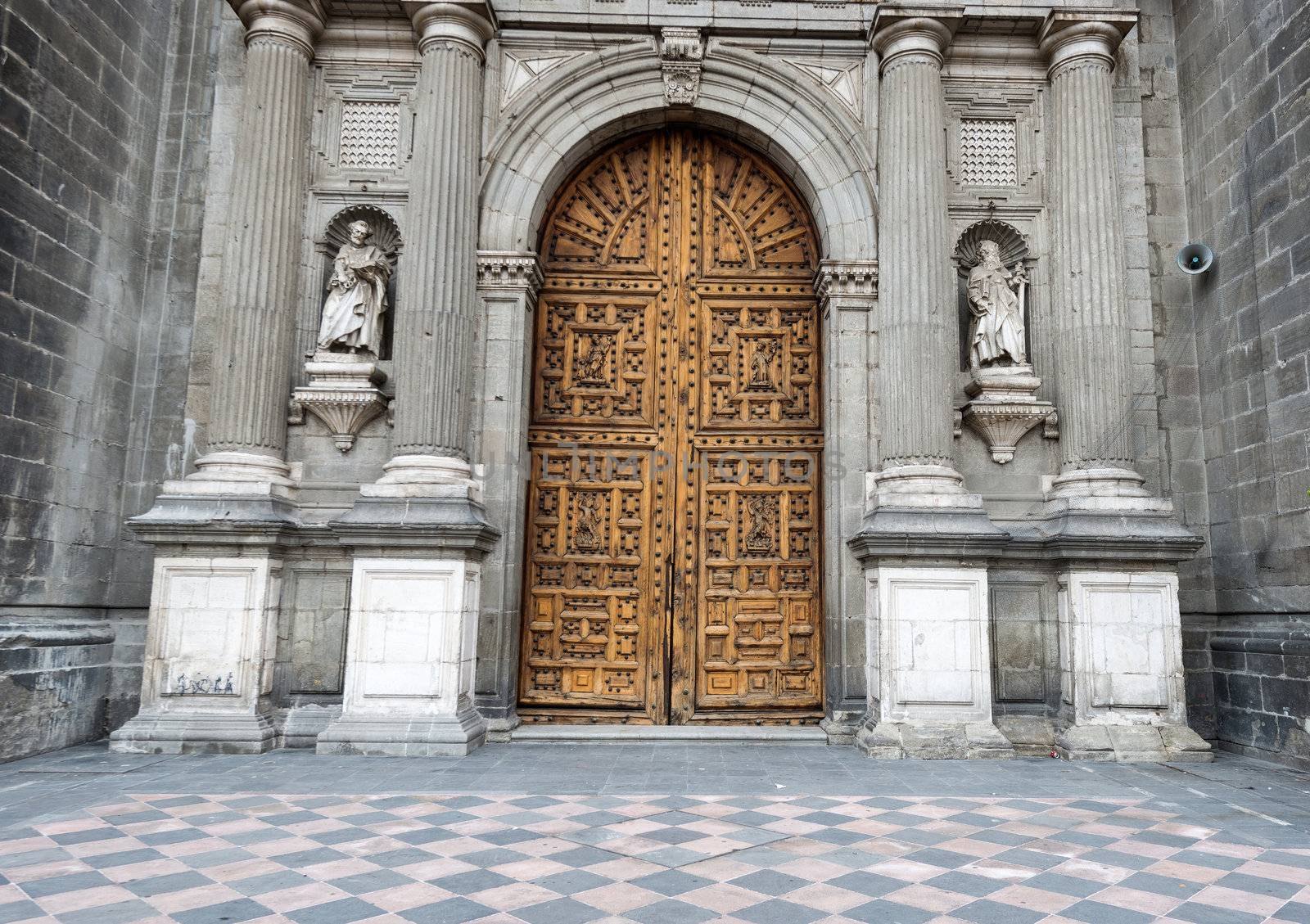 Wooden entrance doors to The Metropolitan Cathedral of the Assumption of Mary of Mexico City. It  is the oldest and largest cathedral in the Americas and seat of the Roman Catholic Archdiocese of Mexico. It is situated atop the former Aztec sacred precinct near the Templo Mayor on the northern side of the Plaza de la Constitución in downtown Mexico City. The cathedral was built in sections from 1573 to 1813 around the original church that was constructed soon after the Spanish conquest of Tenochtitlán, eventually replacing it entirely. Spanish architect Claudio de Arciniega planned the construction, drawing inspiration from Gothic cathedrals in Spain.