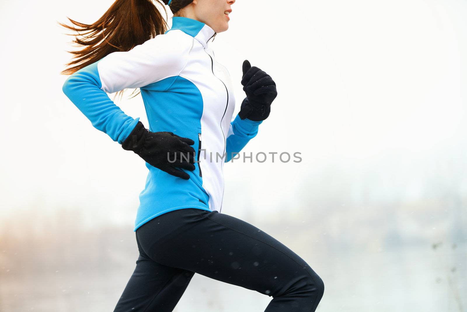 Running athlete woman sprinting during winter training outside in cold snow weather. Close up showing speed and movement.