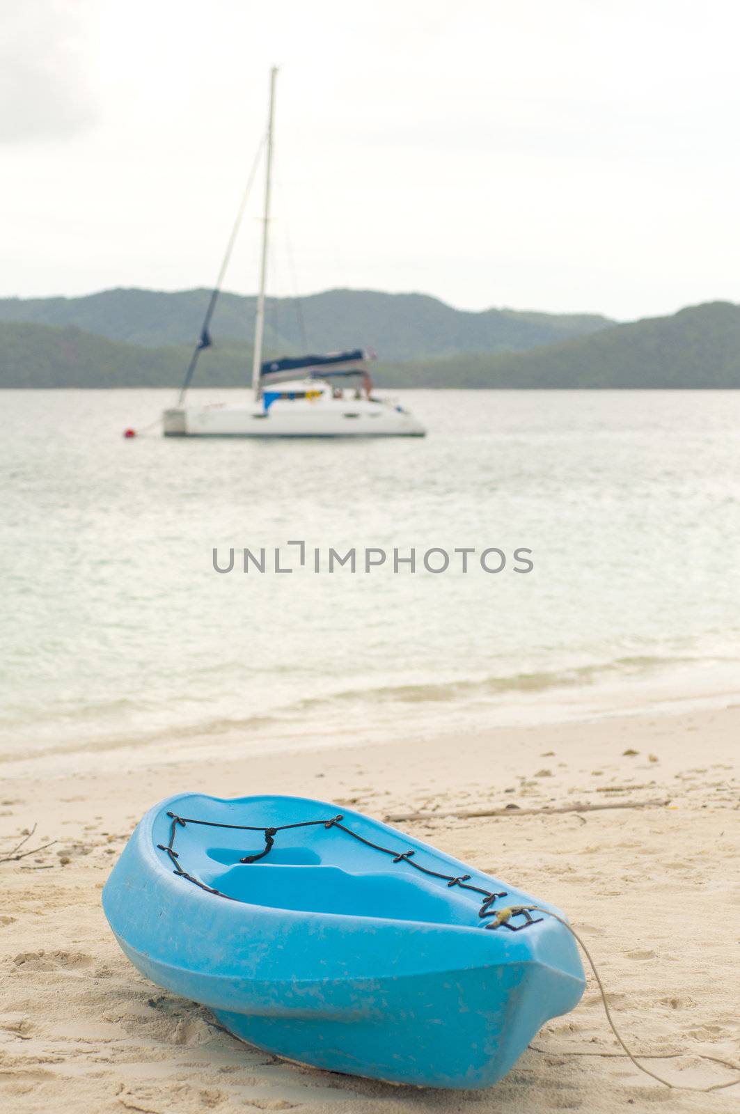 Blue canoe on beach with sailboat on background