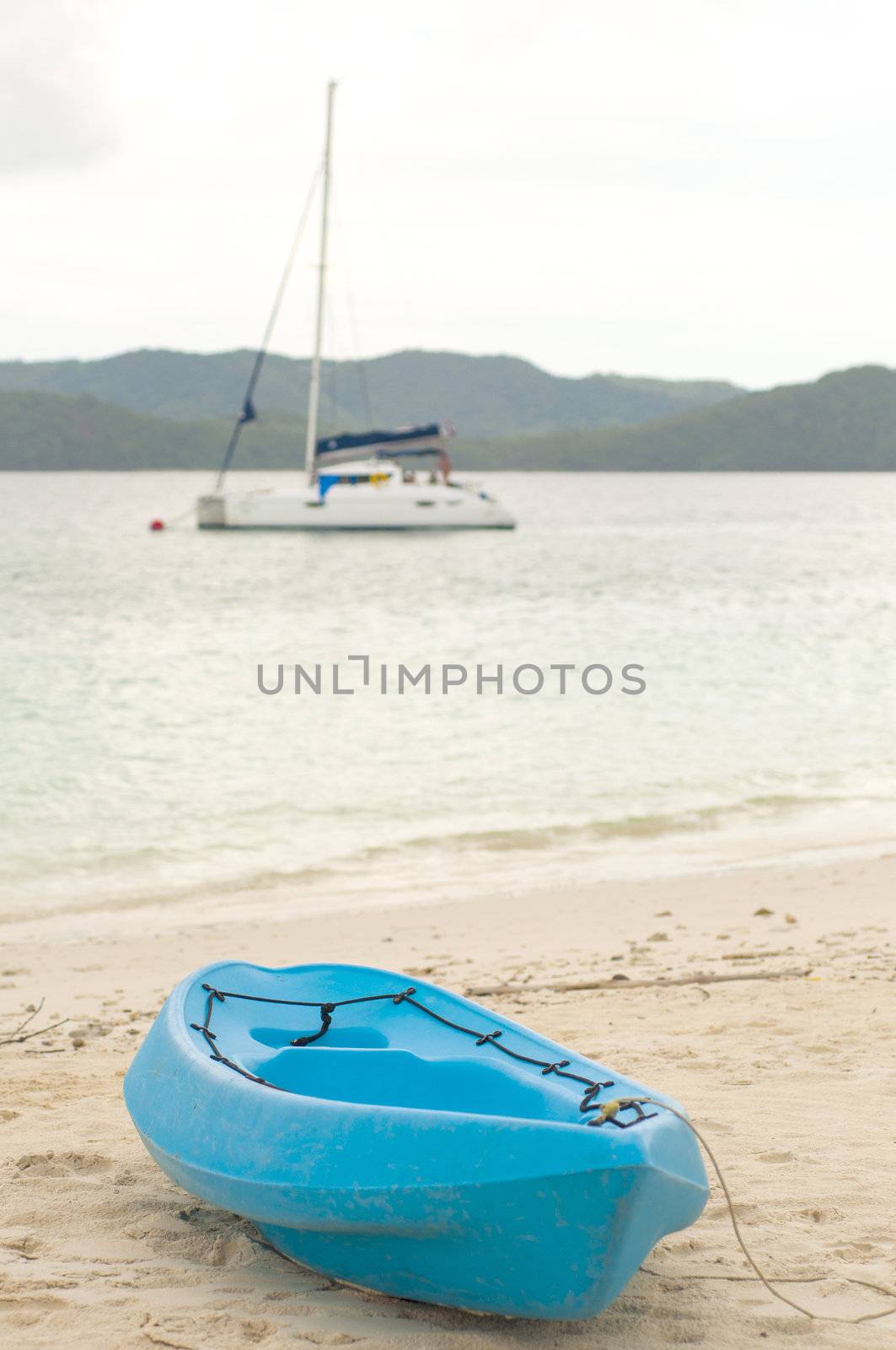 Blue canoe on beach with sailboat on background