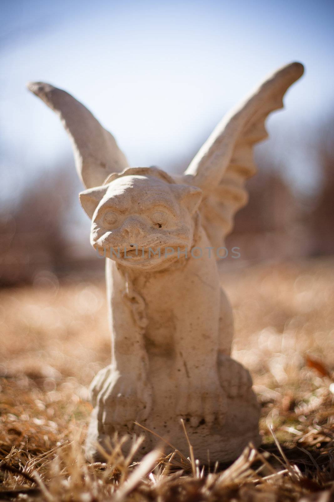 An old gargoyle statue sits in some dead grass.