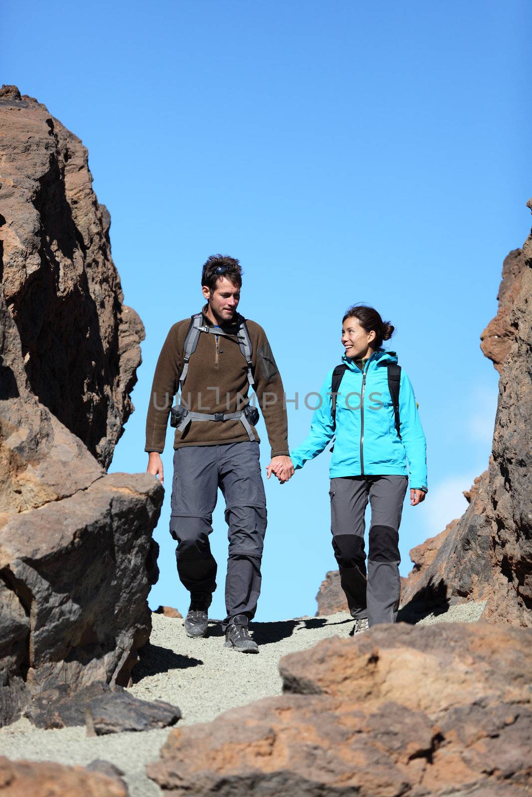 Young couple hiking outdoors holding hands talking during hike trip in beautiful volcano landscape on Teide, Tenerife, Canary Islands.