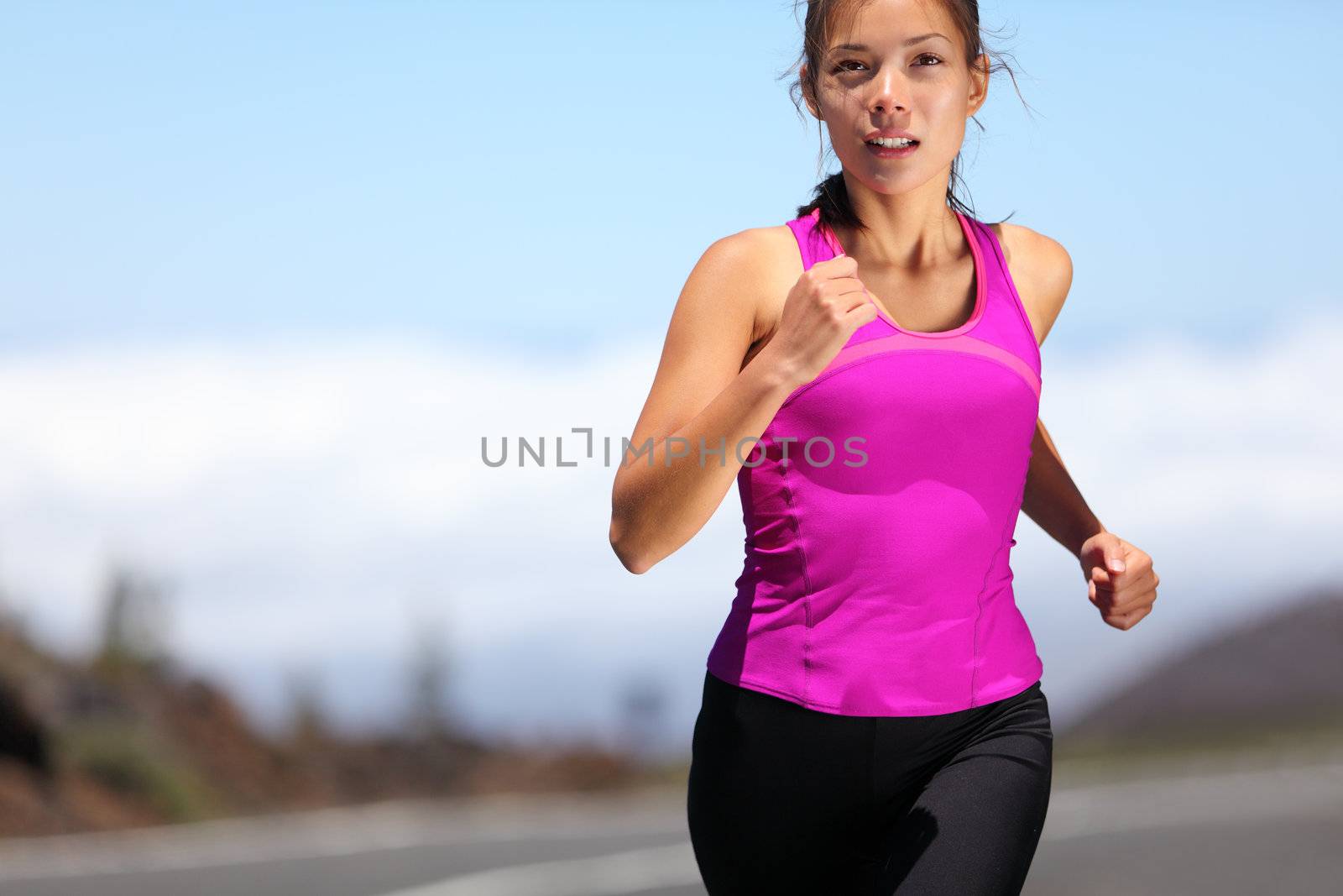 woman runner training for marathon. Female runner in sporty pink tank top jogging on mountain road. Beautiful young mixed race Asian Caucasian female fitness model outside.