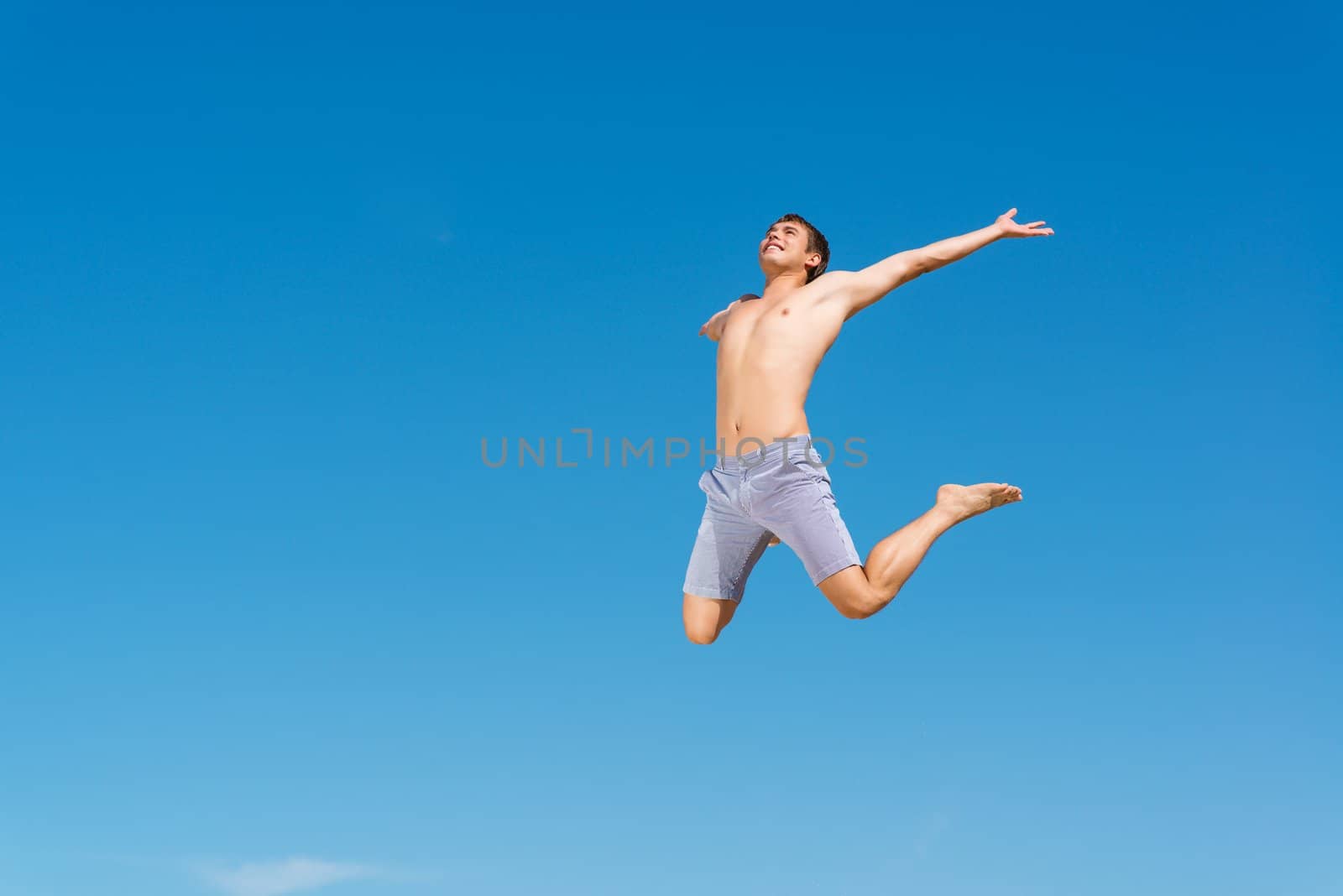 happy young man jumping on a background of blue sky, spreading his hands