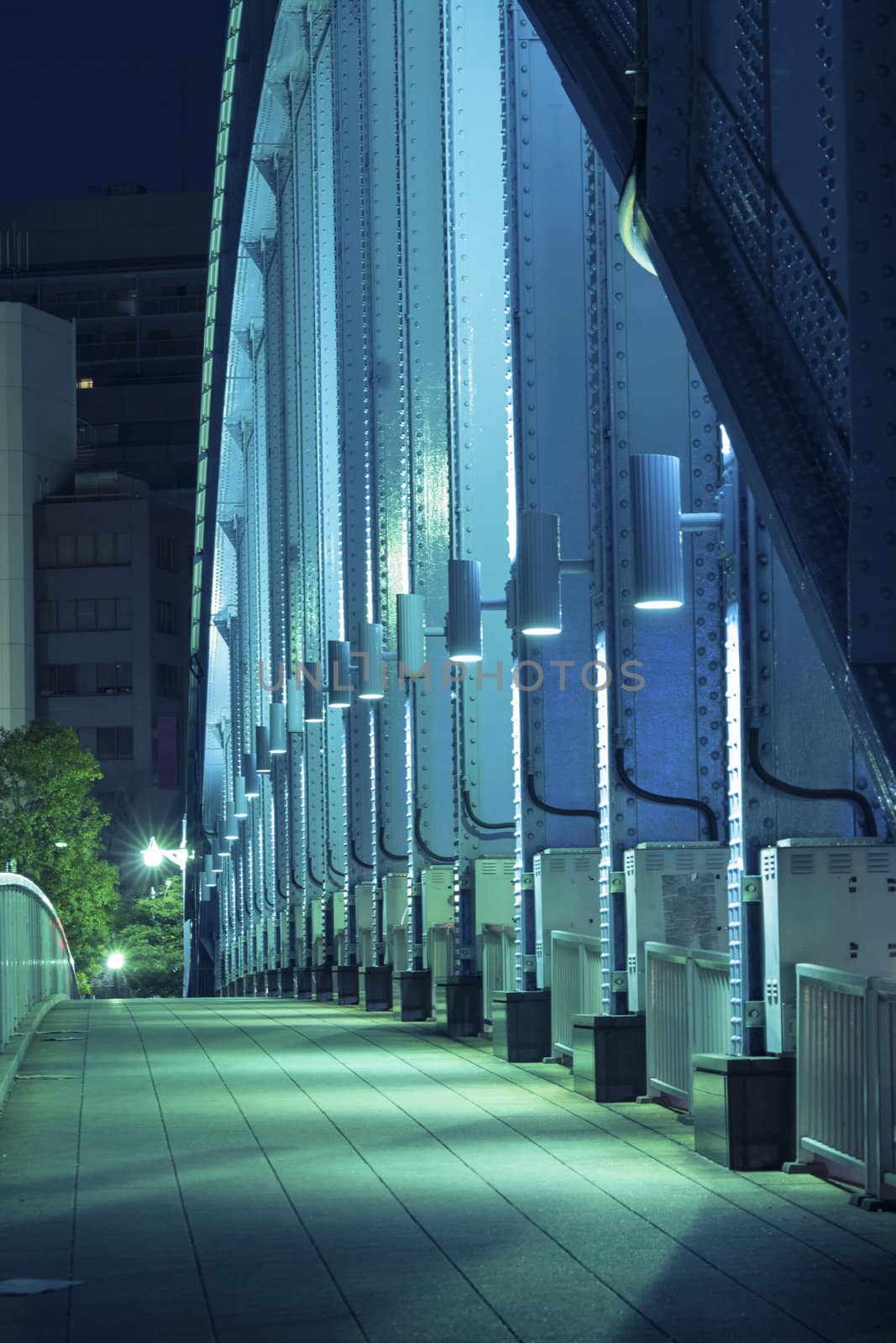pedestrian way along the metallic arc structure of city bridge illuminated by night