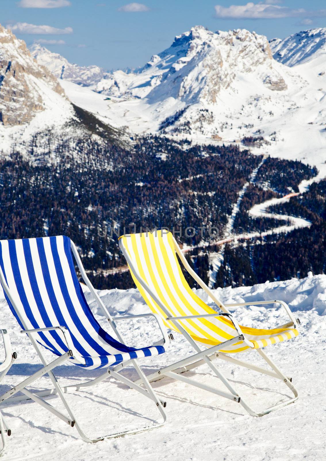 Empty folding chairs on top of a mountain against ski area