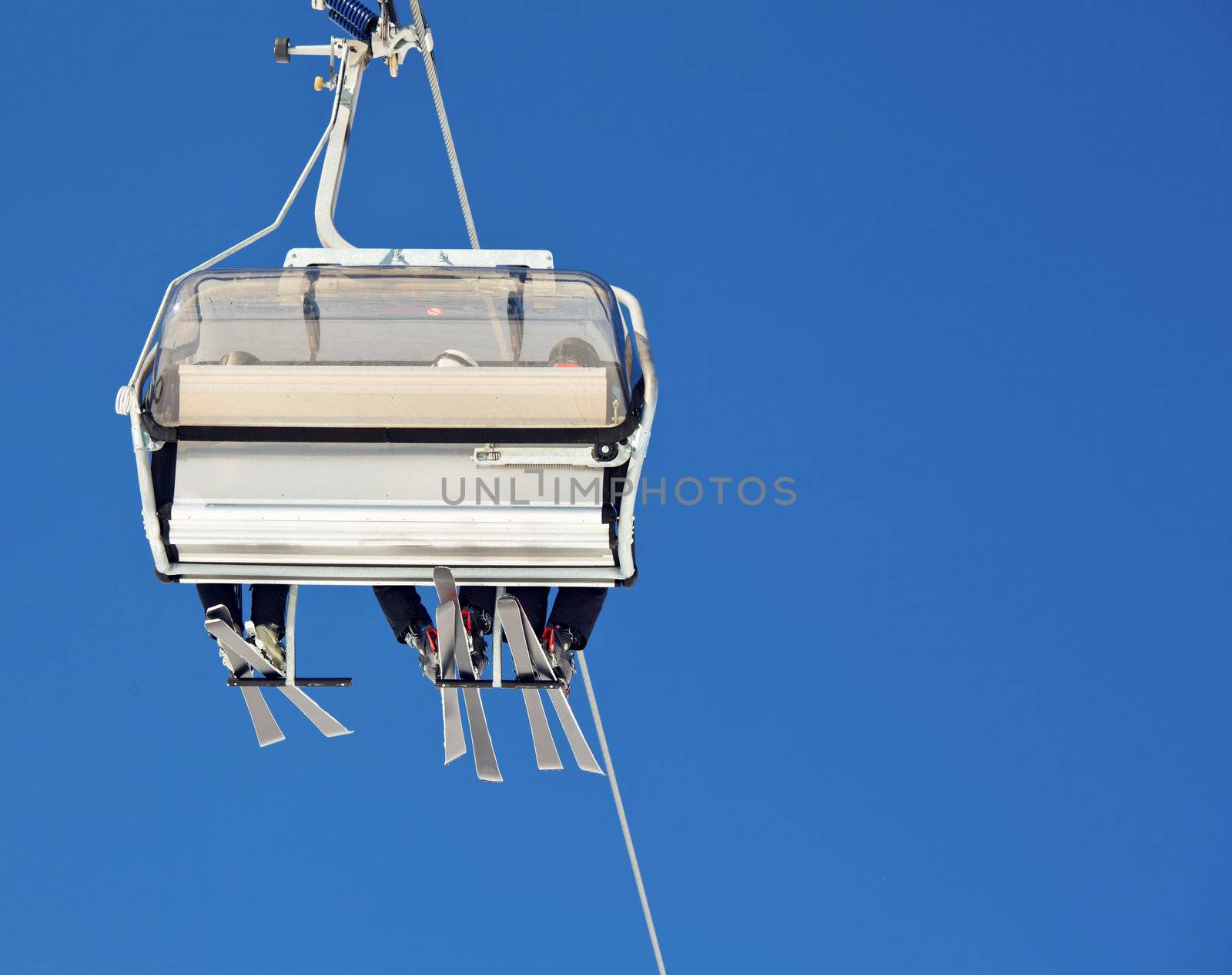 Chair lift with skiers at ski resort against blue sky