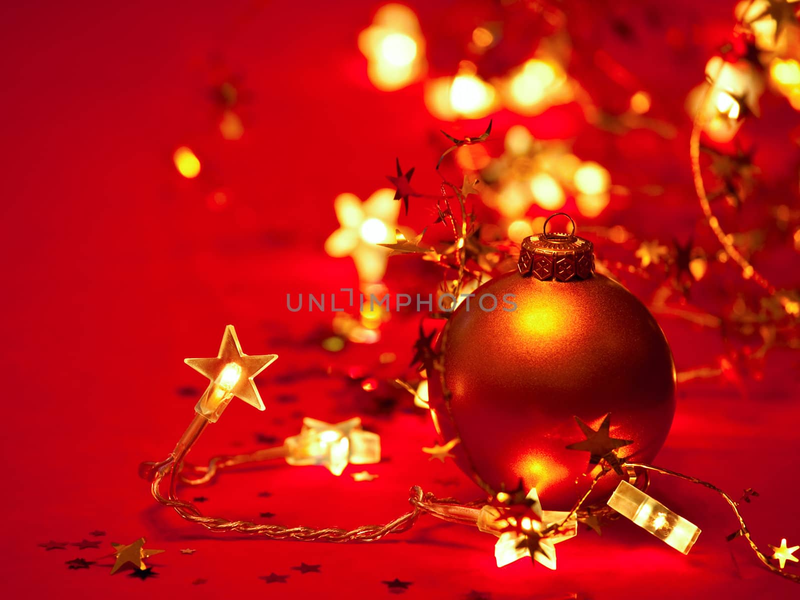 Christmas bauble with star-shaped lights and tinsel on red background, shallow DOF