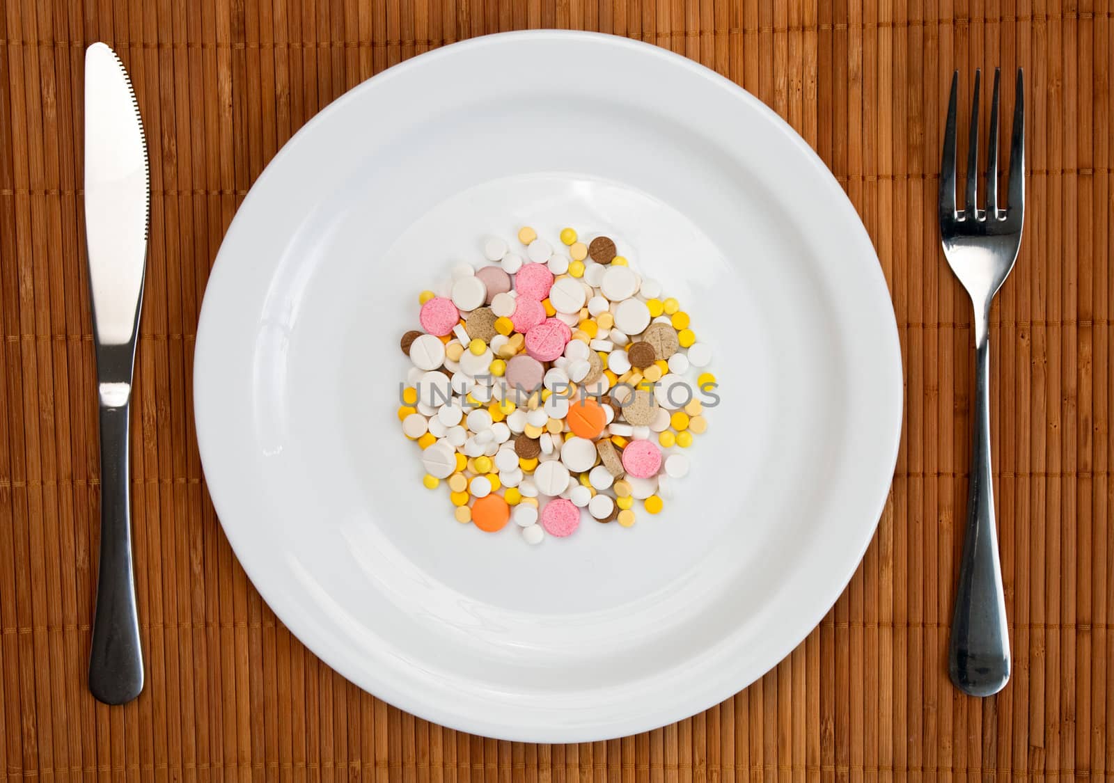 White plate with pills fork and knife on bamboo mat