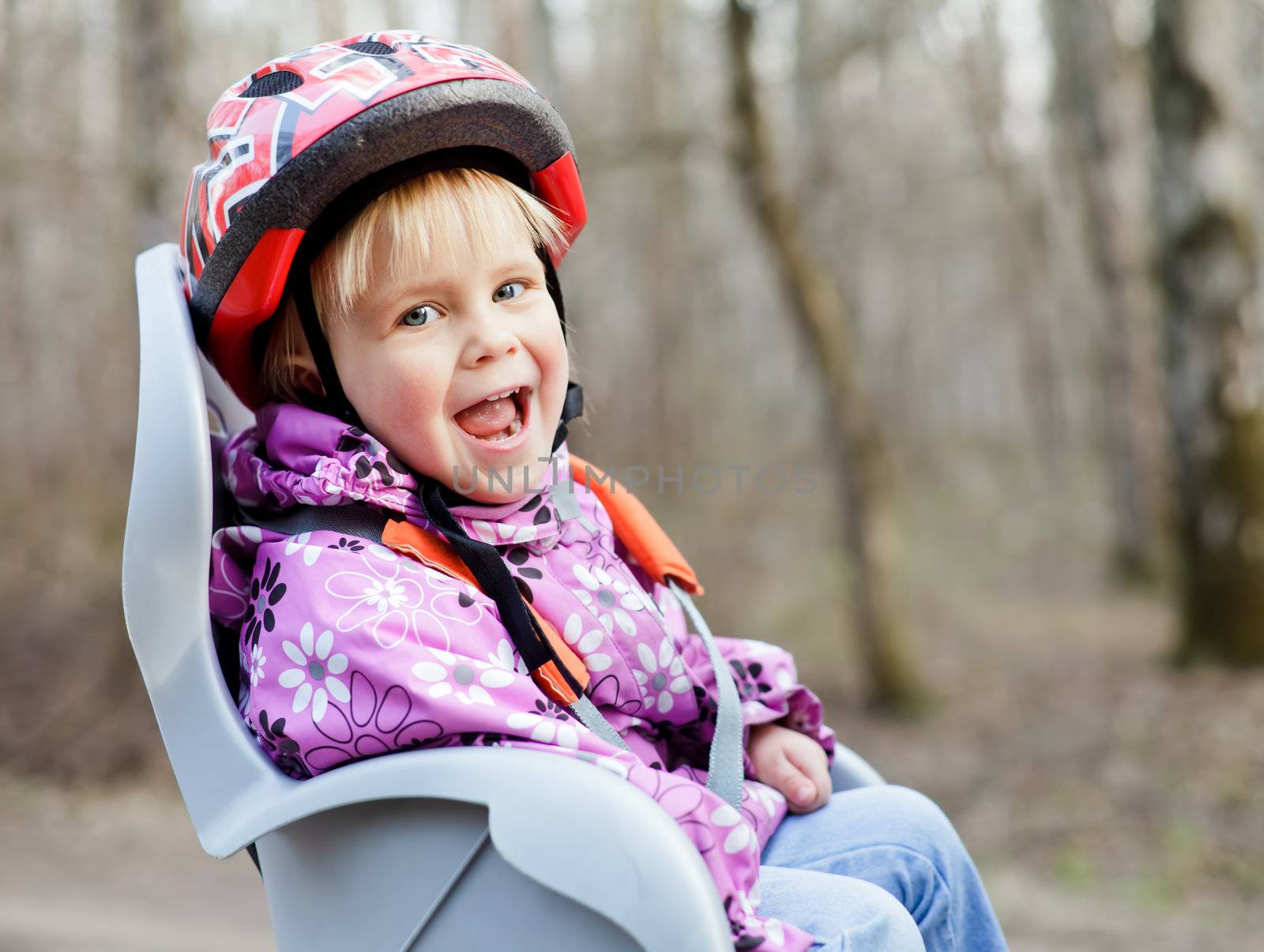 Happy little girl wearing helmet sitting in bycicle child seat