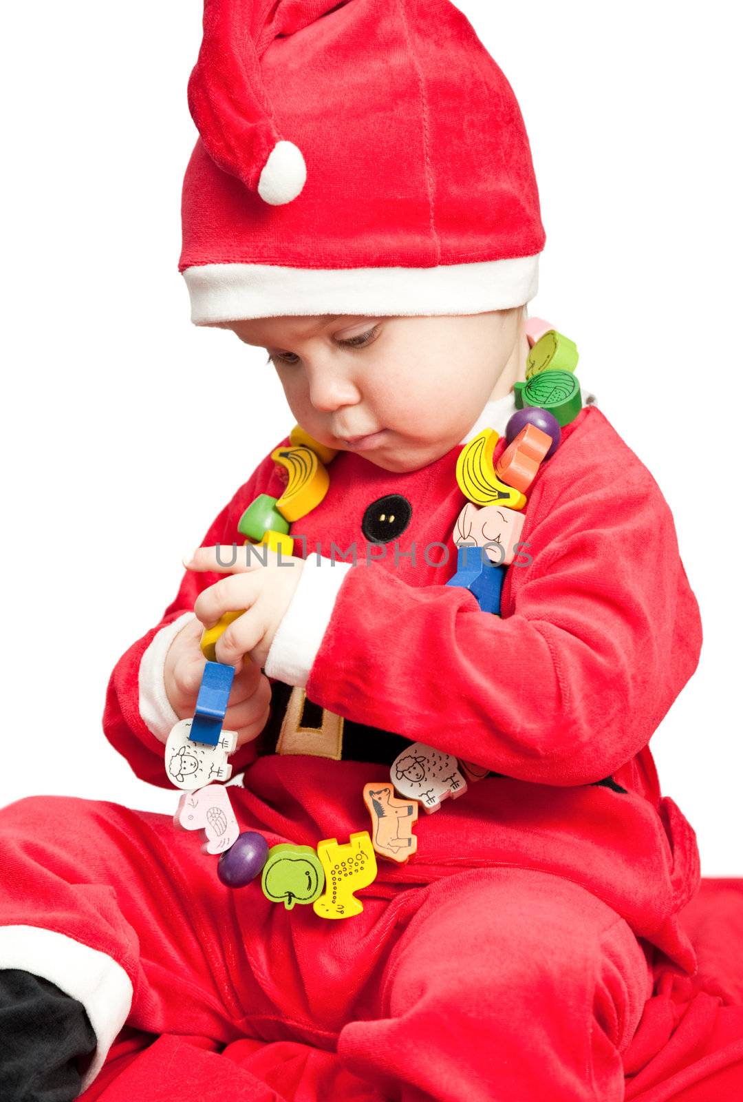 Little baby girl wearing Santa Claus costume playing with wooden beads on white background