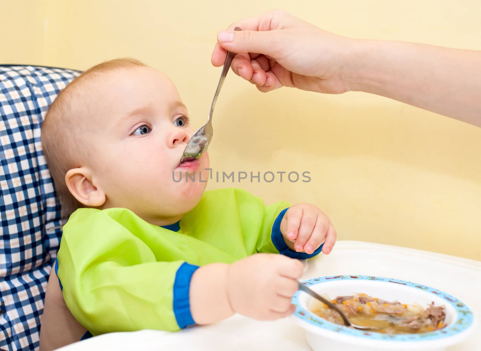 Mother feeding little baby girl in a highchair