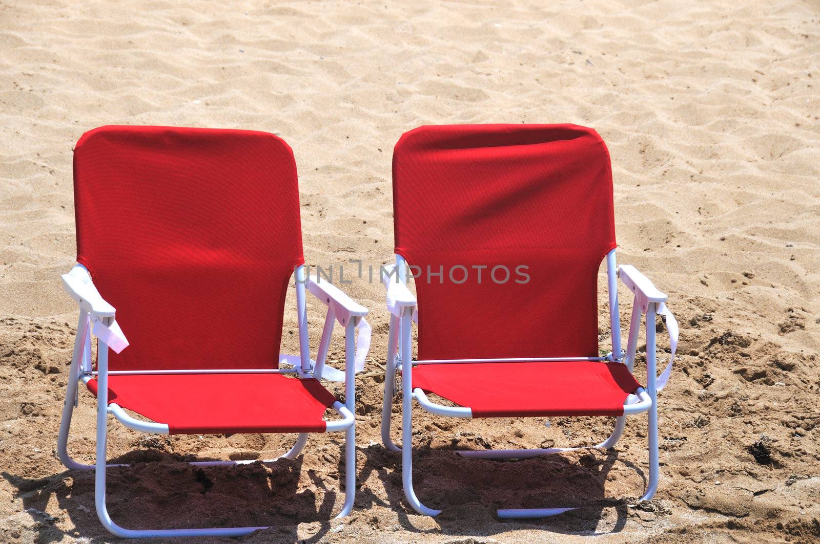 two red folding beach chairs are in the sand on the beach