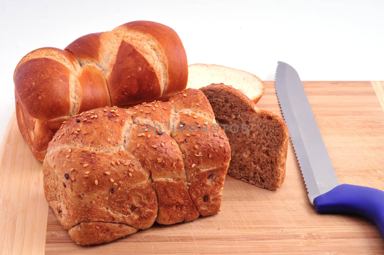 Two rolls of white and dark bread lay on a wooden board beside the knife