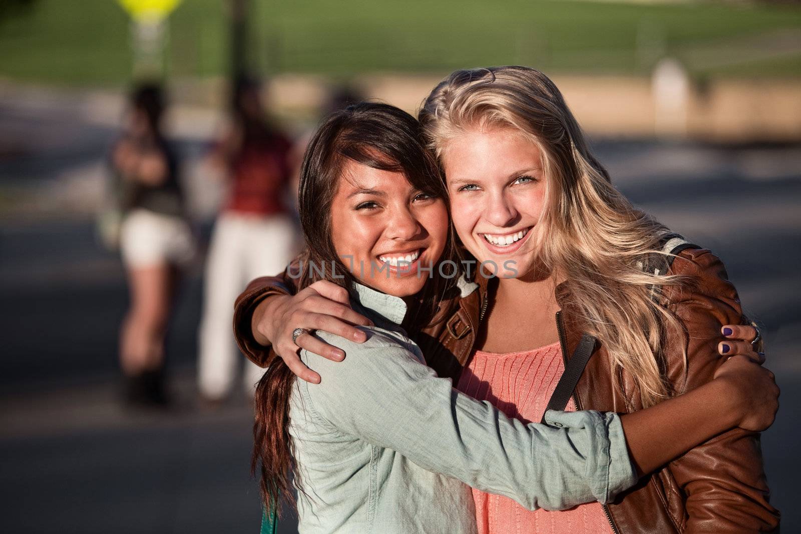 Two hugging female students hugging each other outdoors