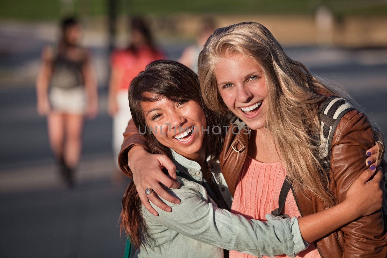 Two laughing female students hugging each other outdoors