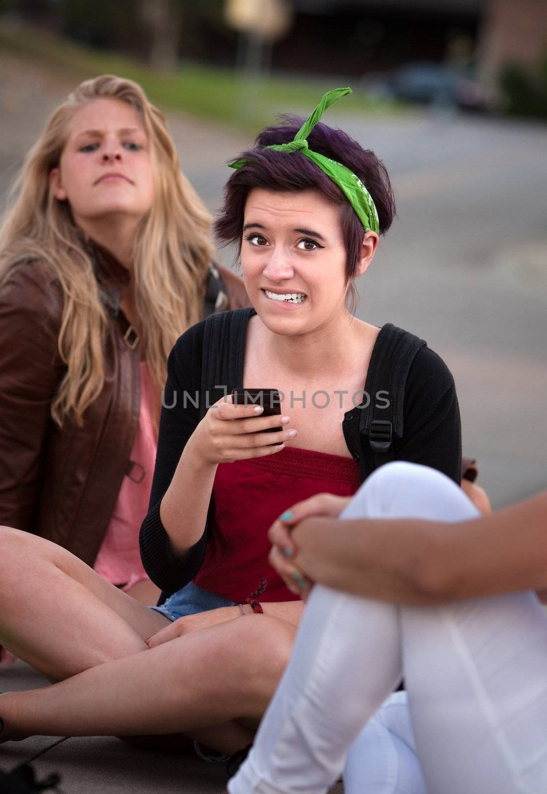 Embarrassed teenage girl holding phone outside with friends