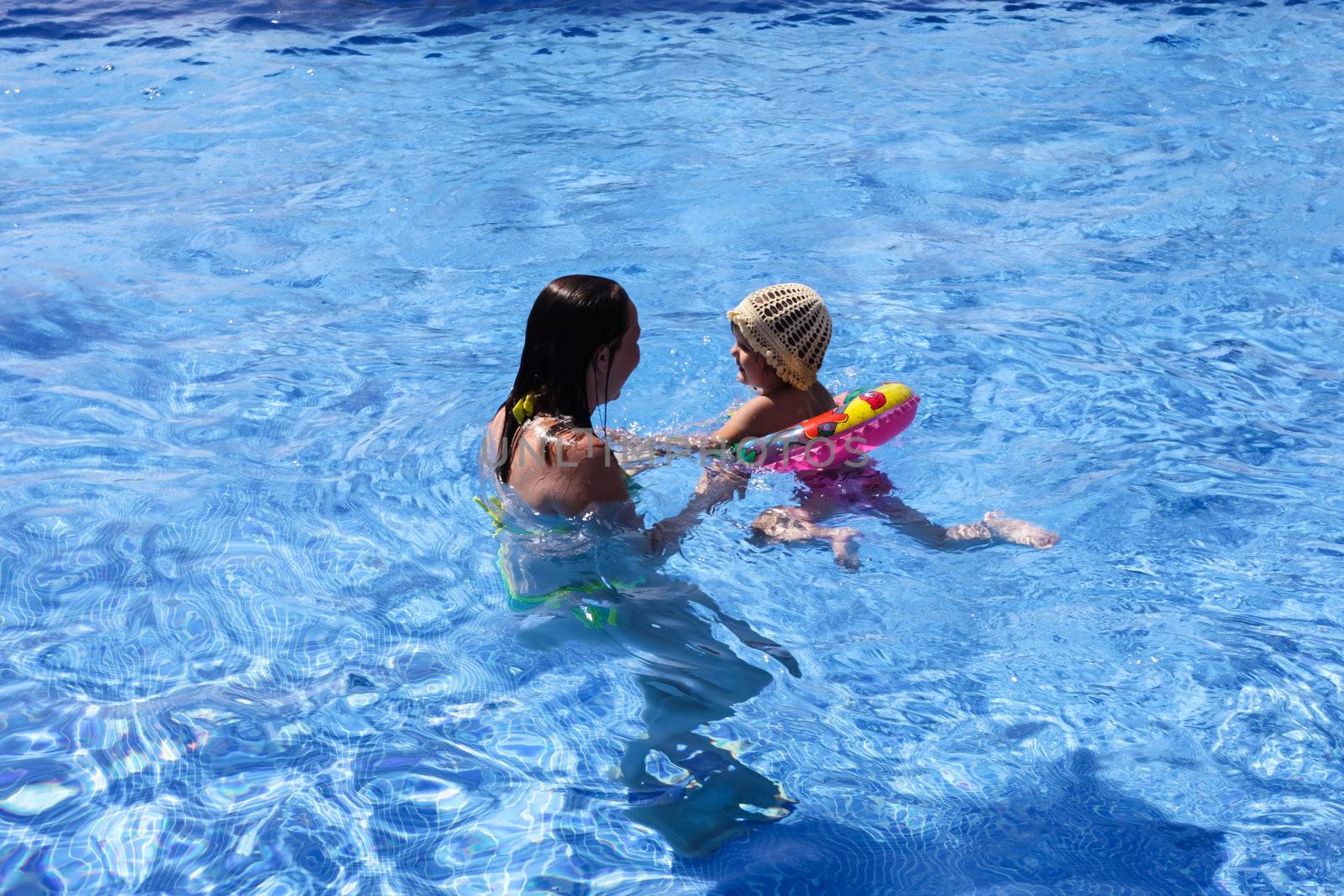 Mother teaching baby girl how to swim in a swimming pool.