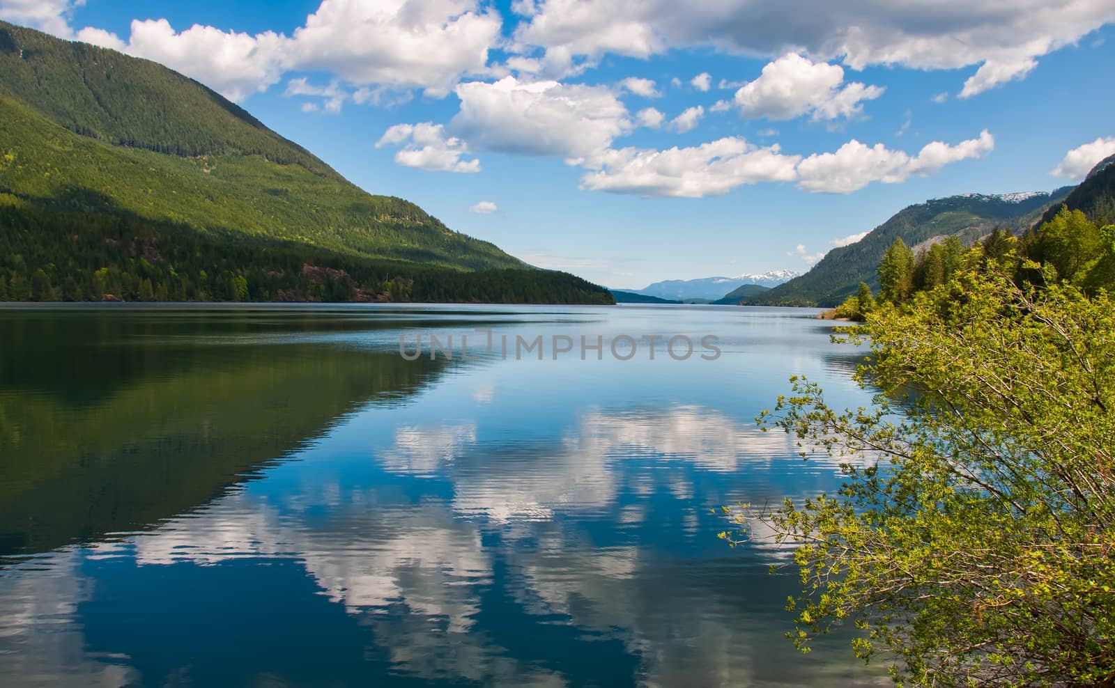 Fluffy clouds reflected in a tranquil lake with mountains in distance