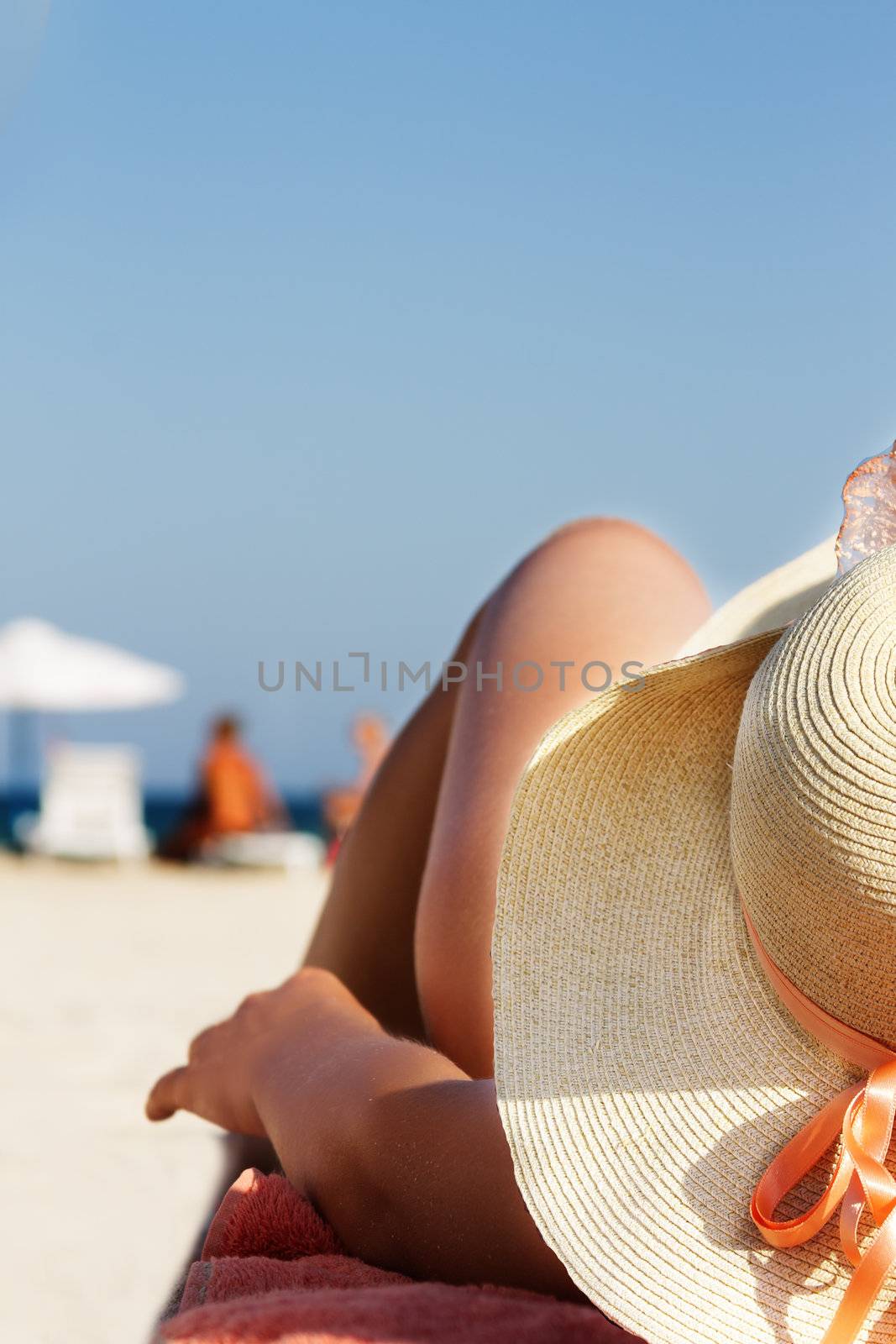 Woman in hat and bikini lying on sandy beach