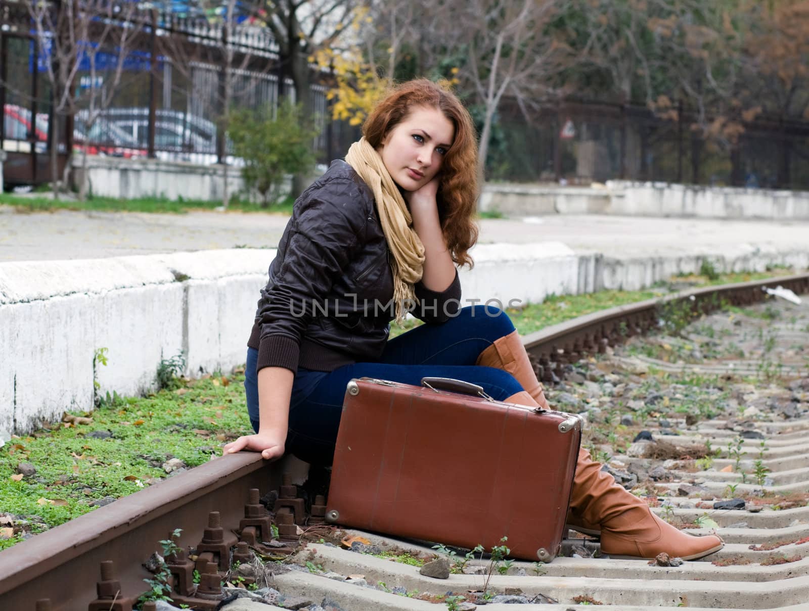 Beautiful girl sitting on a suitcase along the train tracks