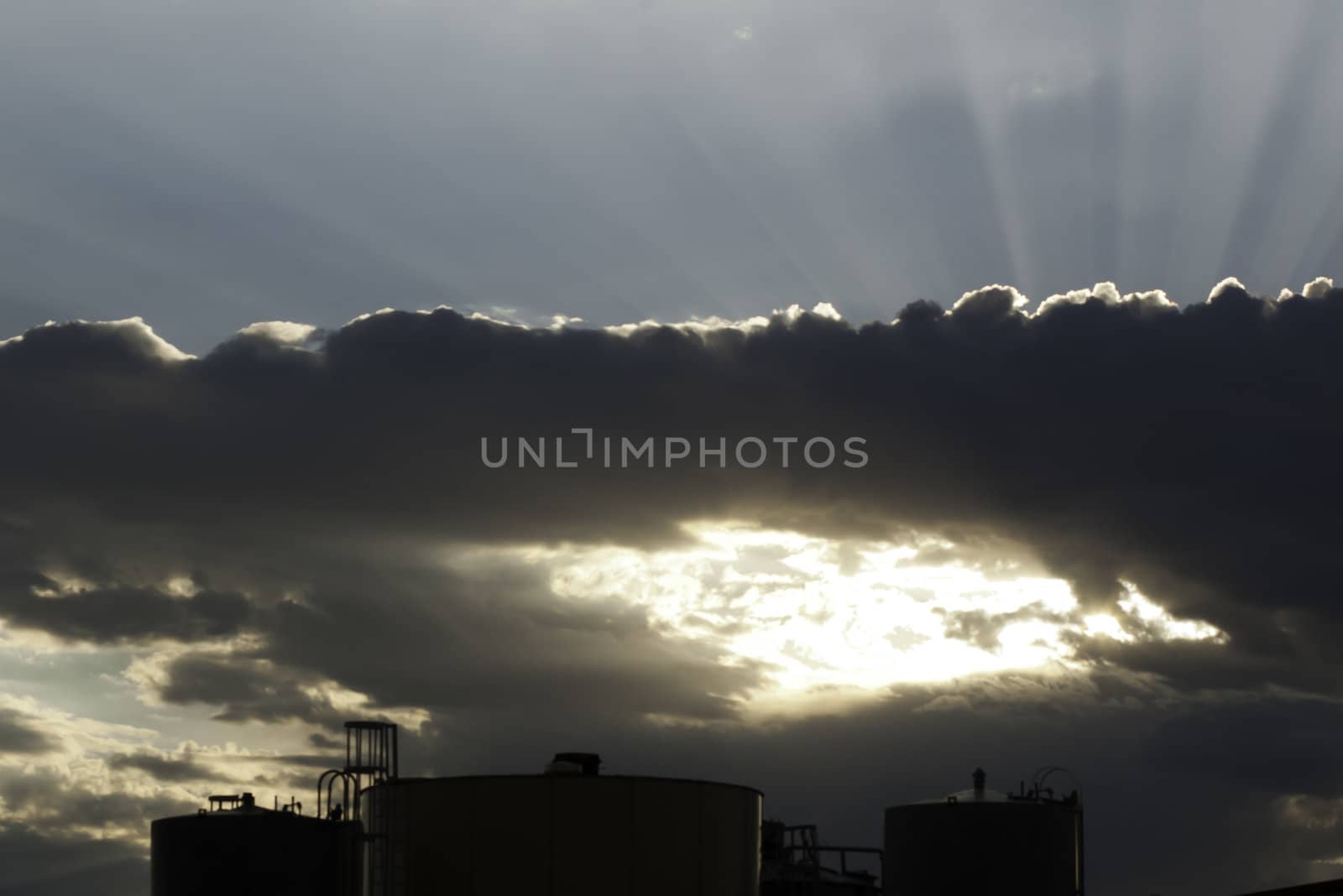 sun rays sunset blue sky through clouds over industrial tanks