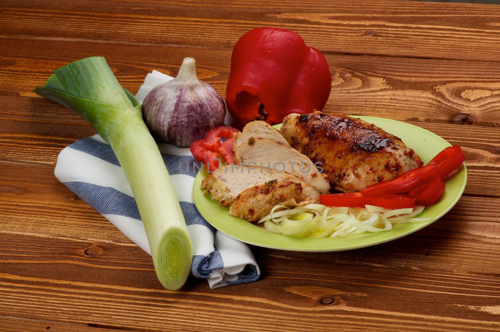 Grilled Chicken Breast with Leek, Garlic and Red Bell Pepper on green plate on wooden background