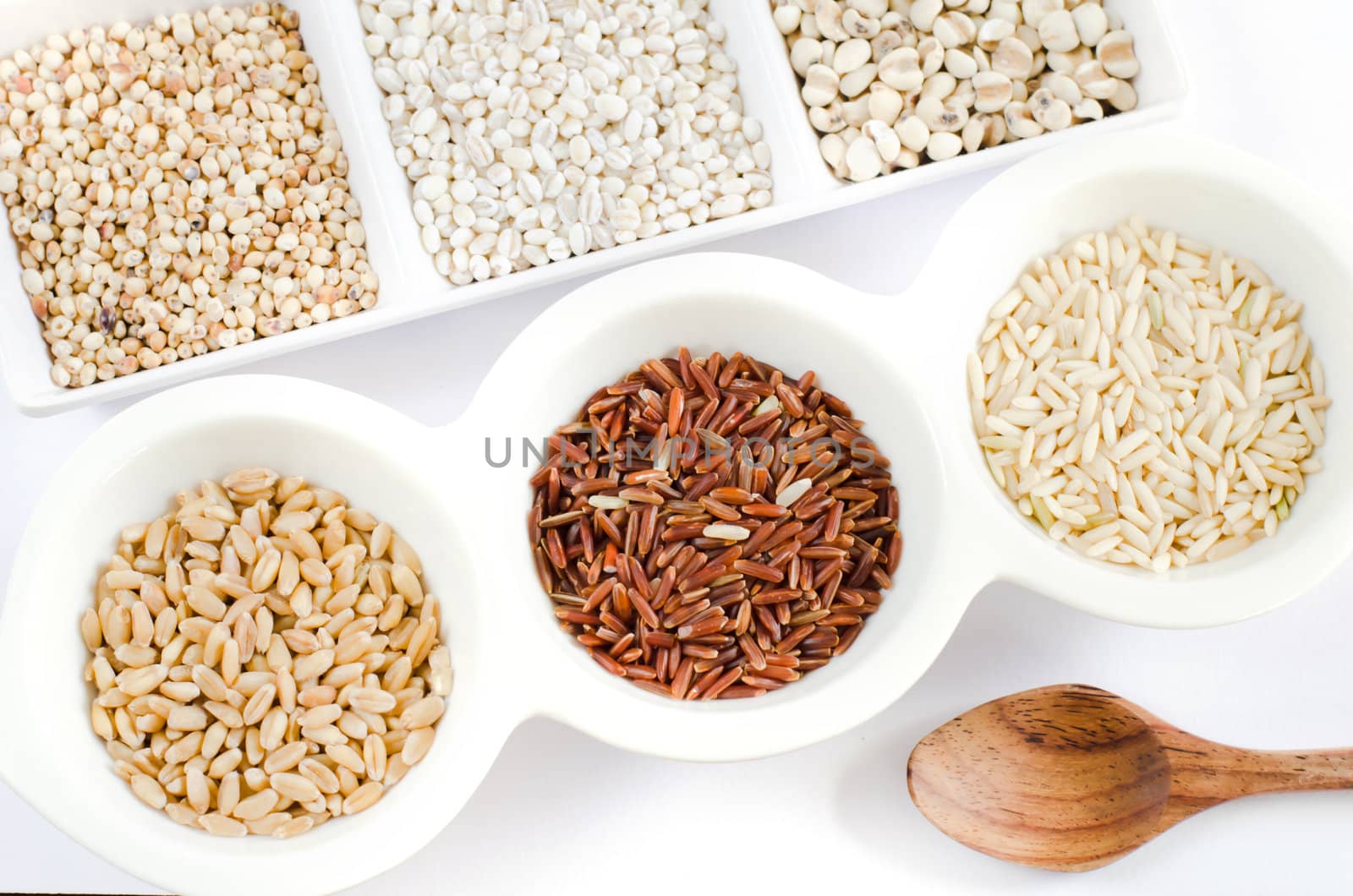top views of grain and wooden spoon ,  rice , red rice , wheat,  job's tears , barley and millet grains on white bowl