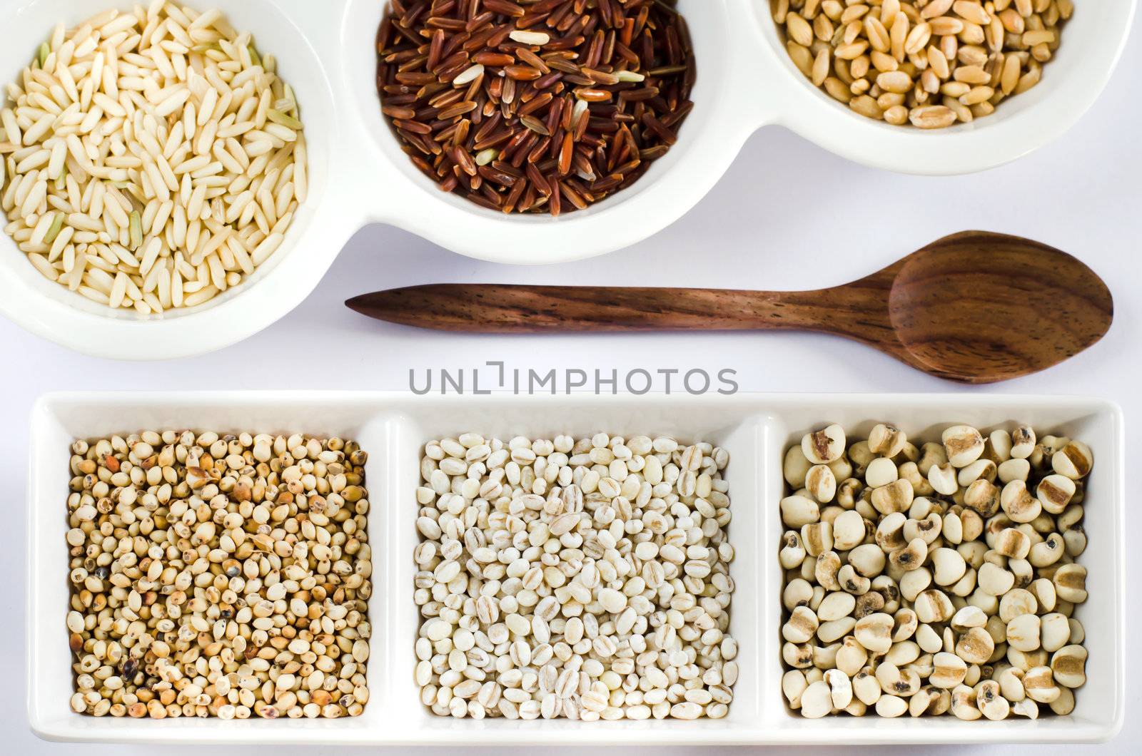 rice , red rice , wheat,  job's tears , barley and millet grains on white bowl , top views of different grain and wooden spoon ,
