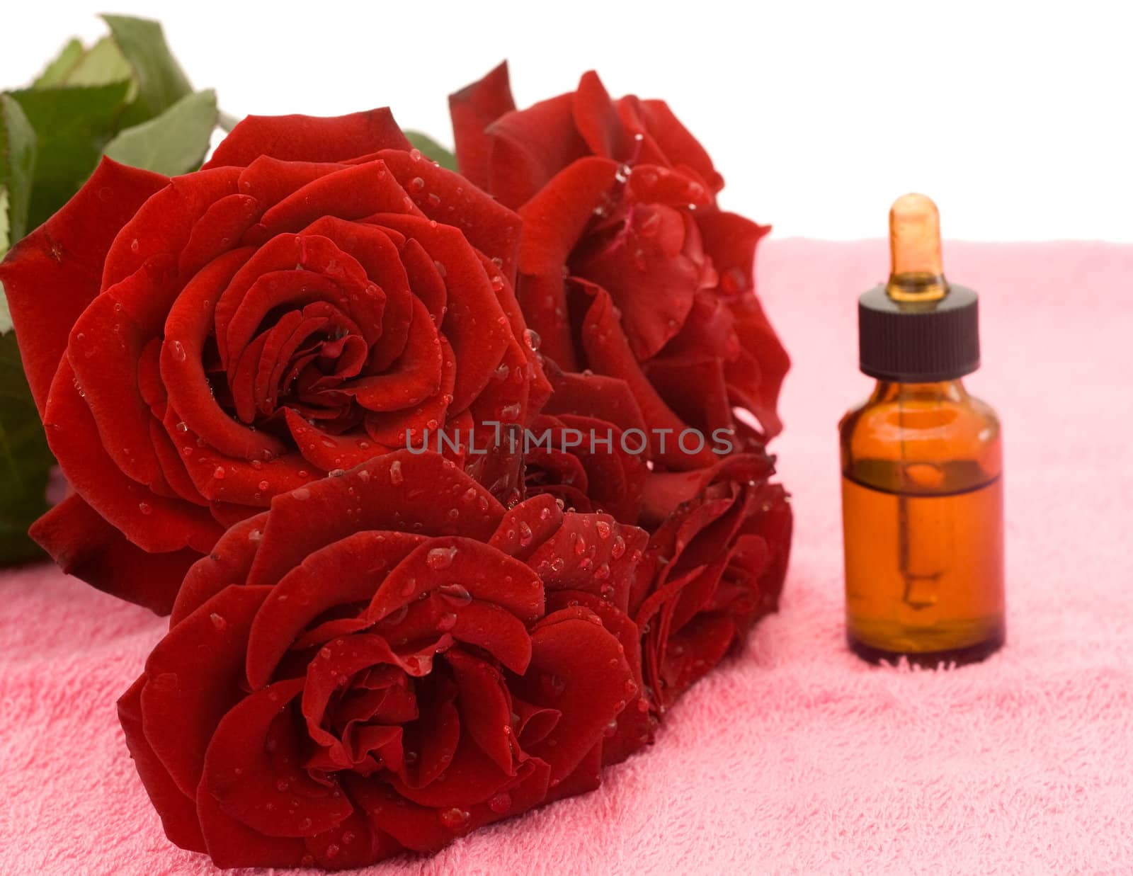 Bouquet of red roses and rose oil on pink towel
