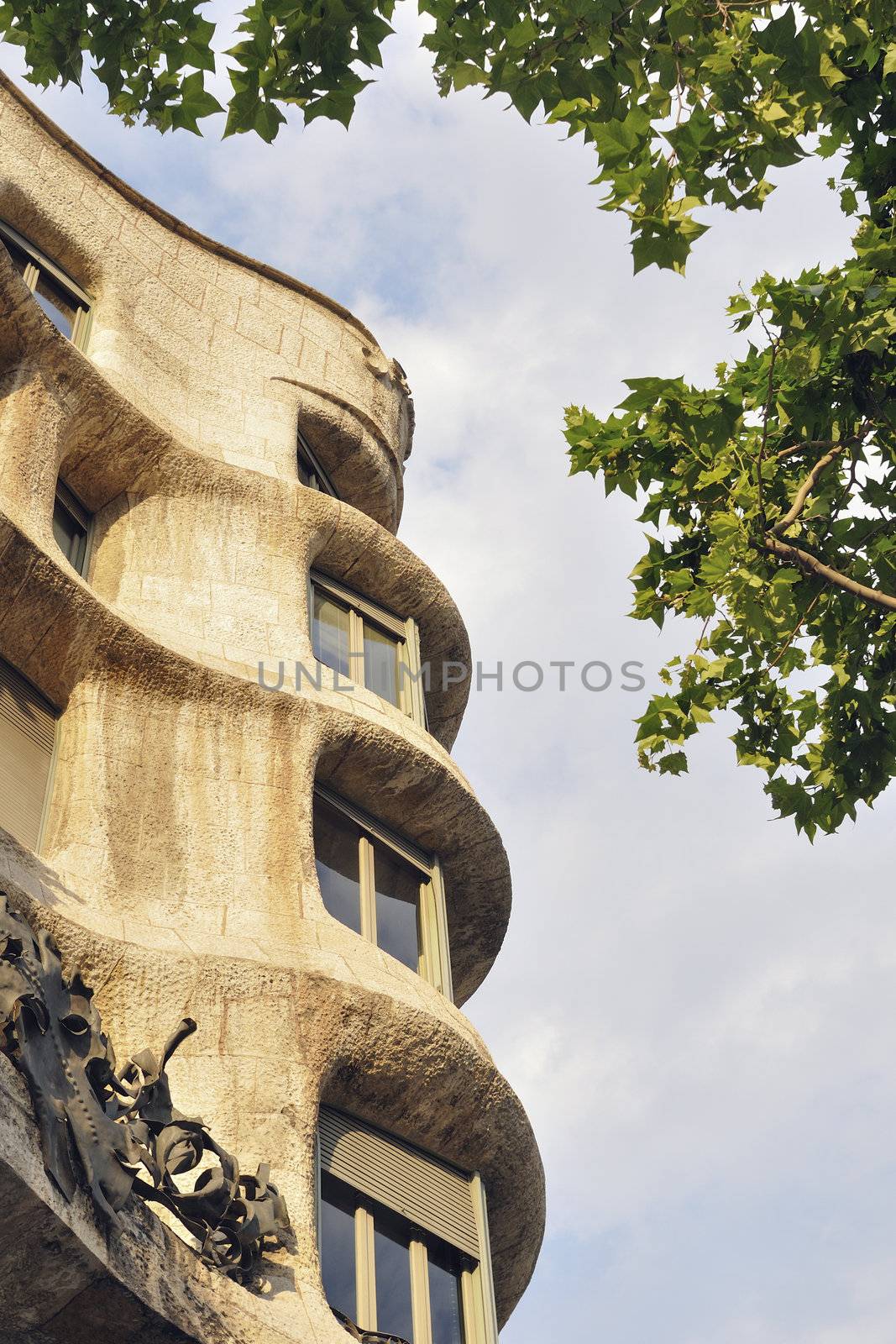 exterior of Famous modernist building La Pedrera by architect Antonio Gaudi  in Barcelona, Spain between green platan leafs