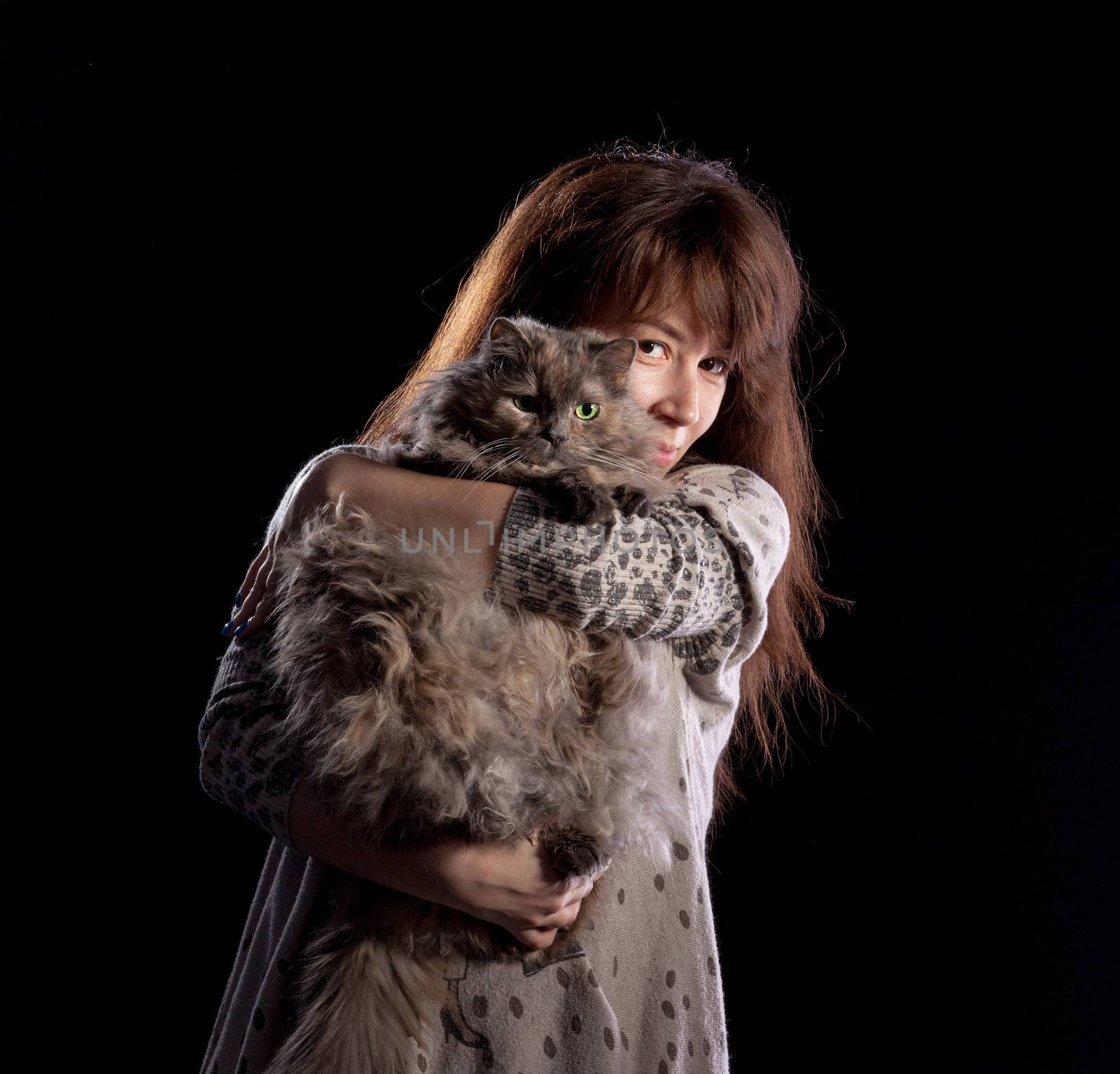 Young beautiful smiling woman holds fluffy cat, on black background