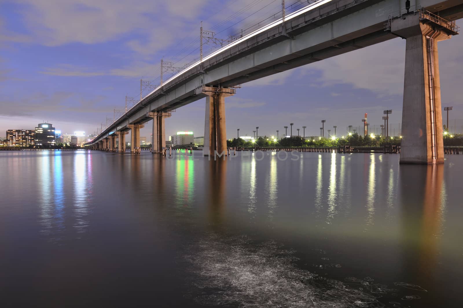 big railway bridge on the tall concrete columns over Tokyo Bay waters by night time