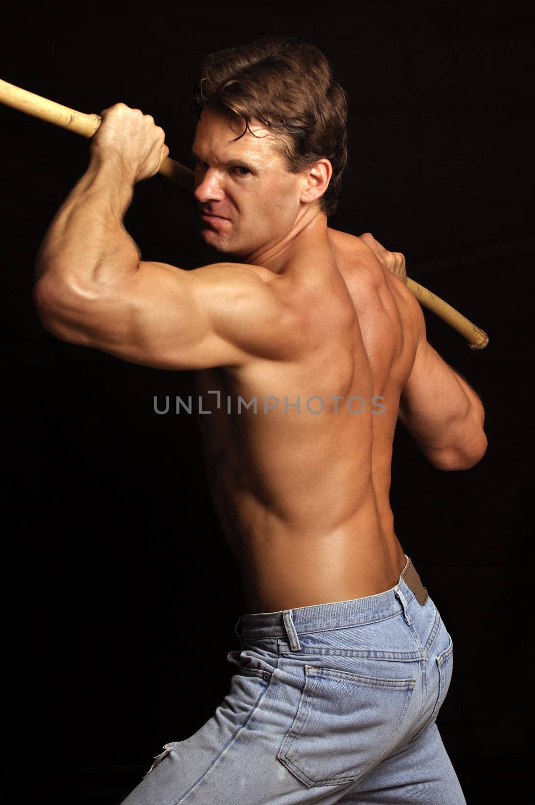 Shirtless muscular man attacks victim with bamboo stick on black background