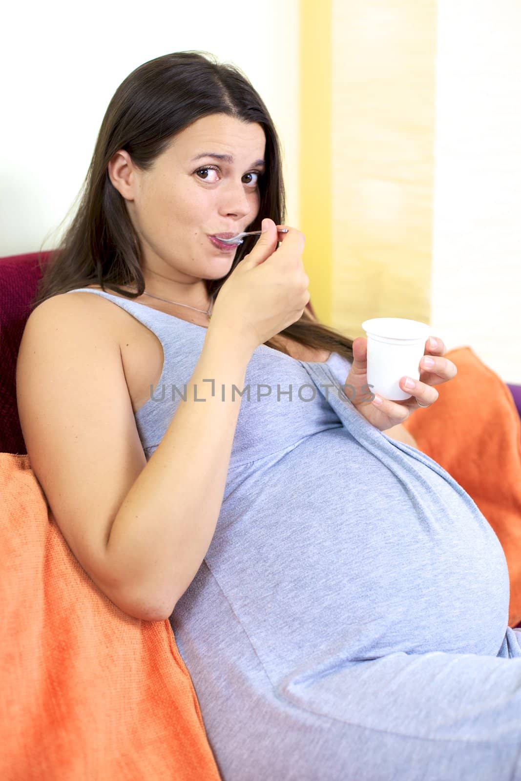 Happy pregnant woman eating yogurt at home by fmarsicano