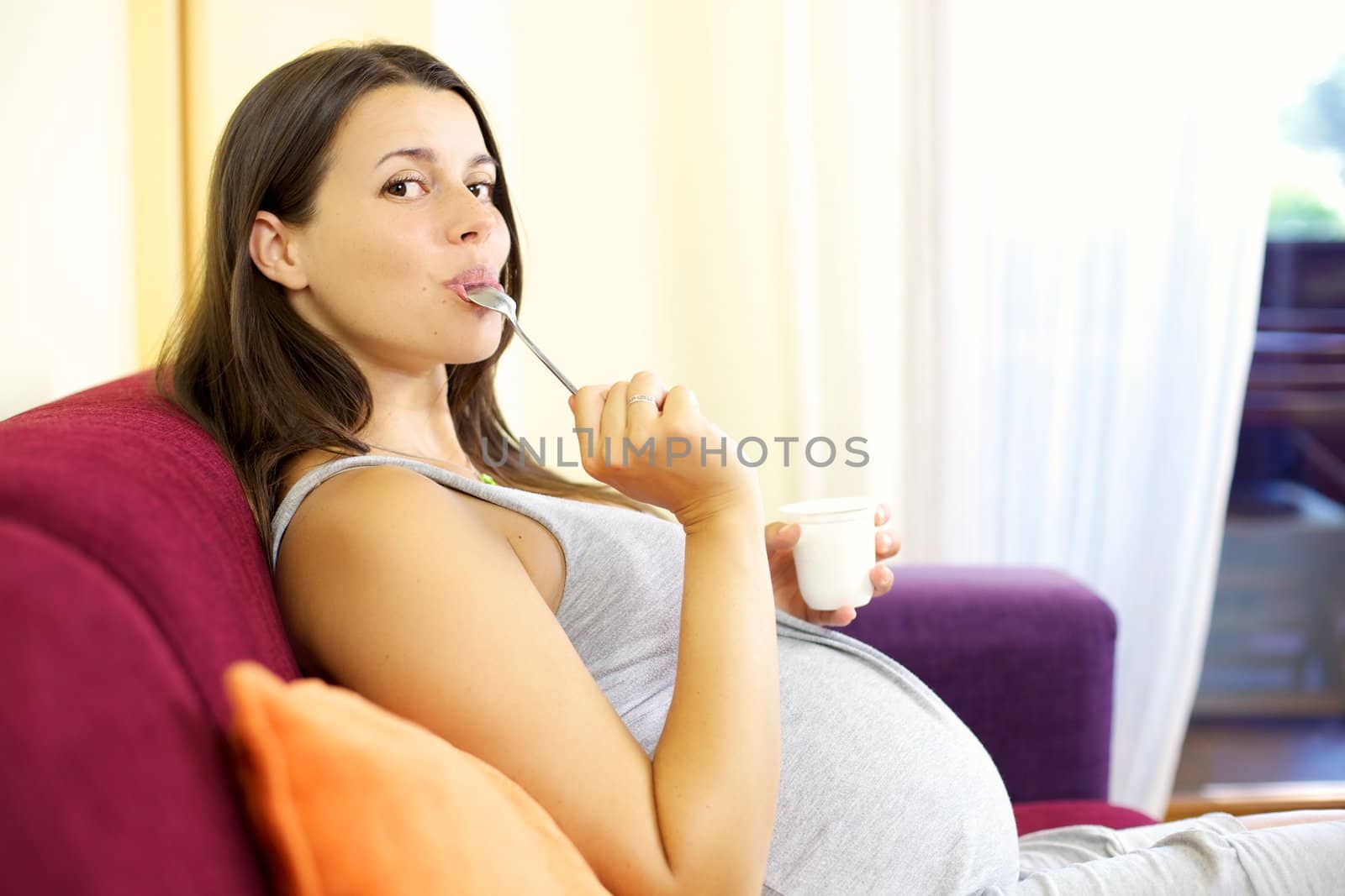 Happy pregnant woman licking spoong with yogurt by fmarsicano