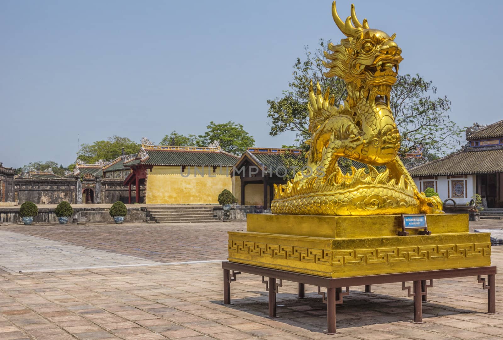Shining golden statue under blue skies with sino-vietnamese architecture in background.