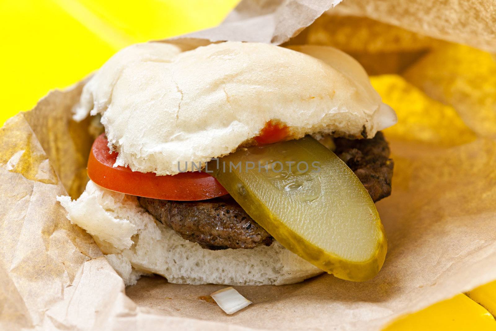 Homemade hamburger with pickle and tomato in paper wrapper