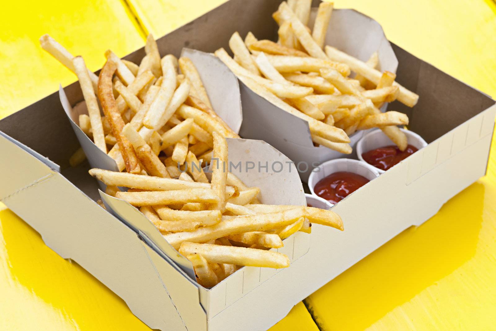 Portions of french fried potatoes with ketchup in cardboard take-out box