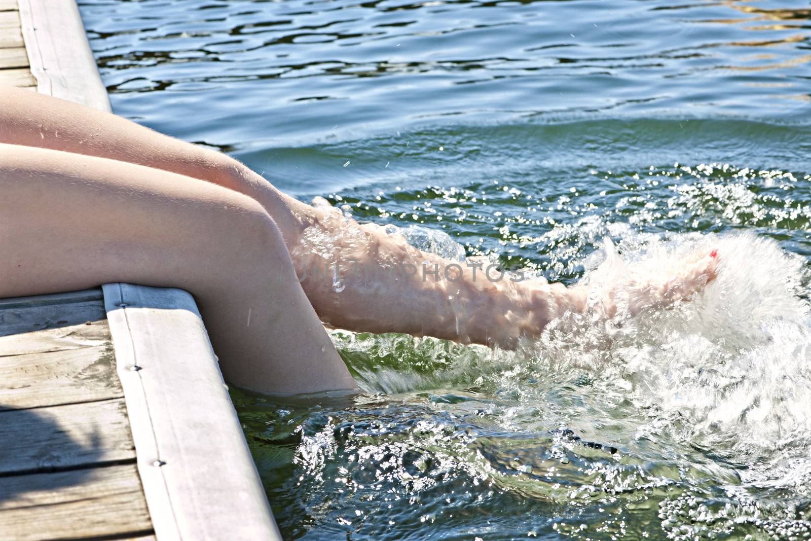 Girl sitting on dock splashing bare legs in lake