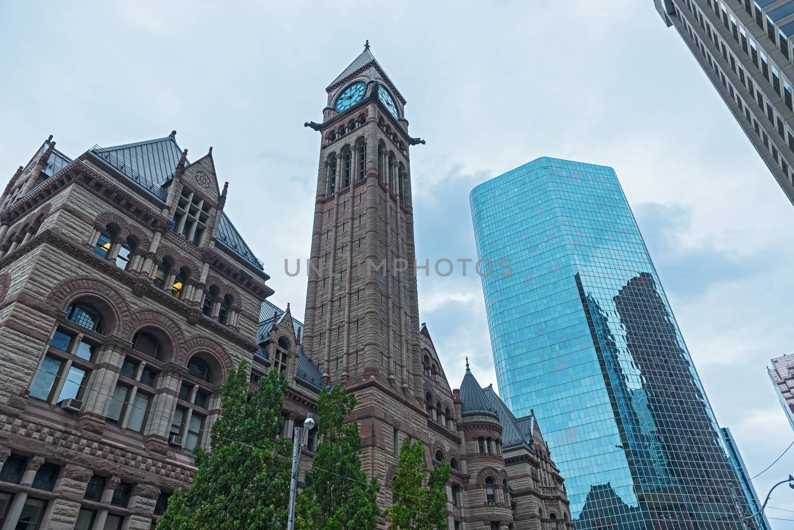 A view of the Old City Hall in Toronto with modern office buildings around it under blue skies.