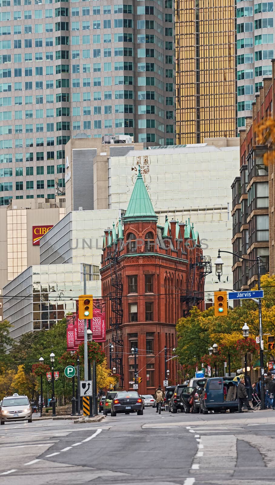 Toronto, Canada - October 07, 2012: Toronto’s landmark Flatiron Building, a restored late 19th century Victorian office building built by architect David Roberts Jr. In the background on the left, the two towers . Picture is taken in  the afternoon, while cars are moving along  Front Street East. Trees on the right start to change their colours from green to yellow. 