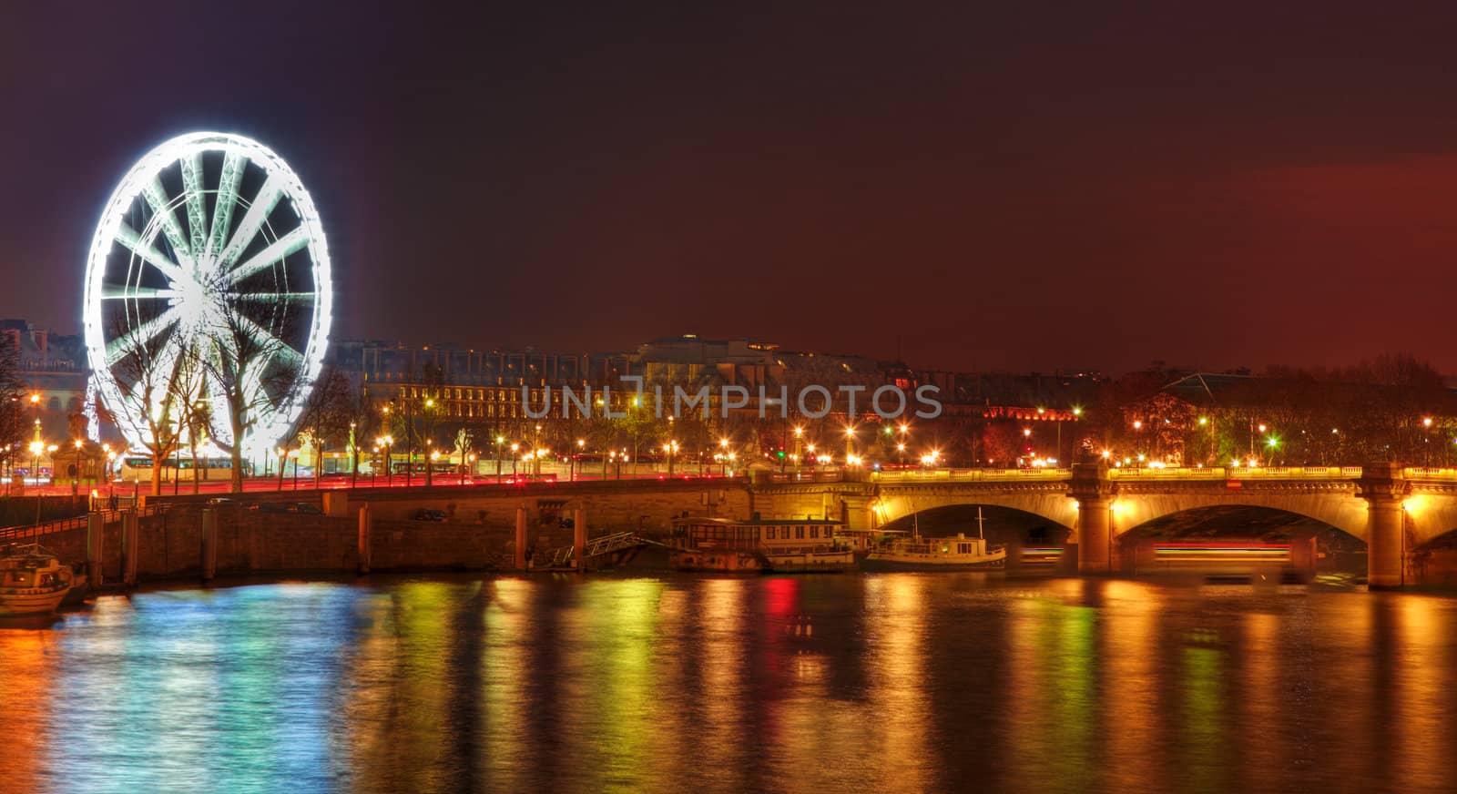 Image of the illuminated Ferry Wheel located in Place de la Concorde and colorful light reflections in the river Seine in Paris.