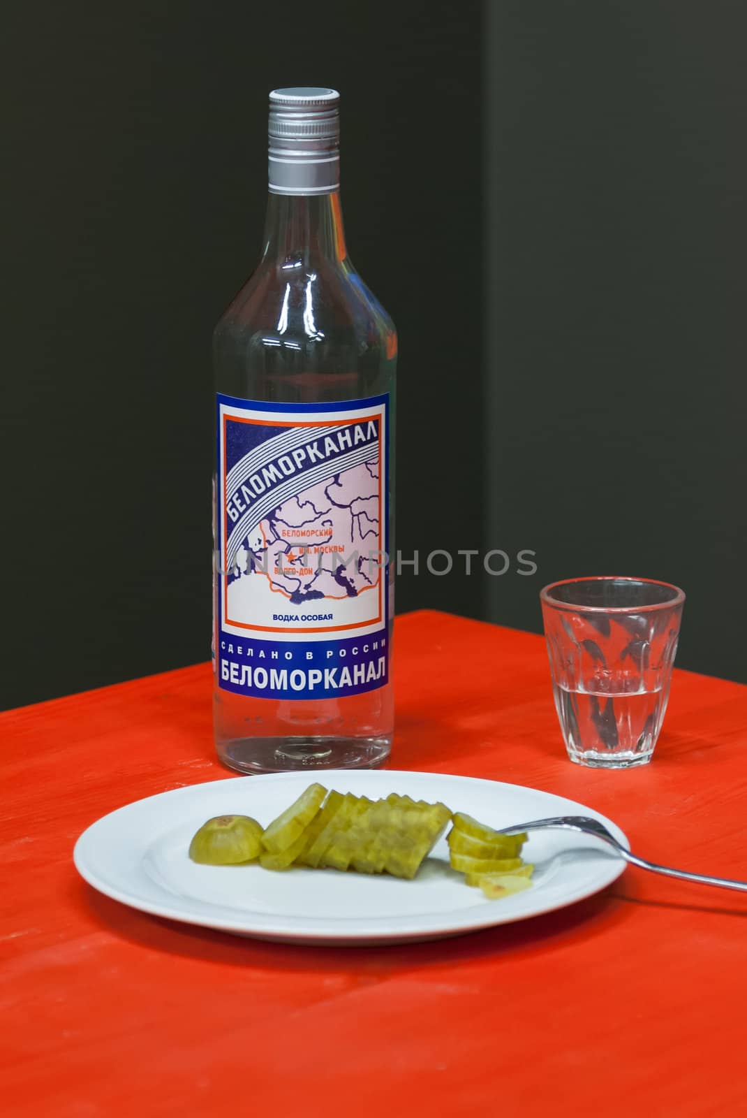 a bottle of vodka "White Sea" pickles and a glass on a table with red tablecloth