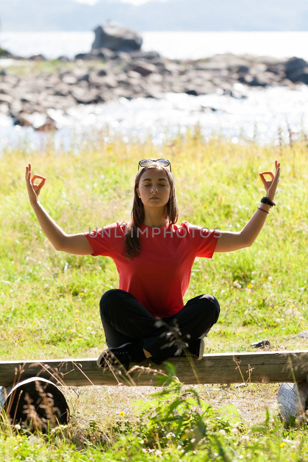 Beautiful girl in a red dress sitting on a bench in the lotus position